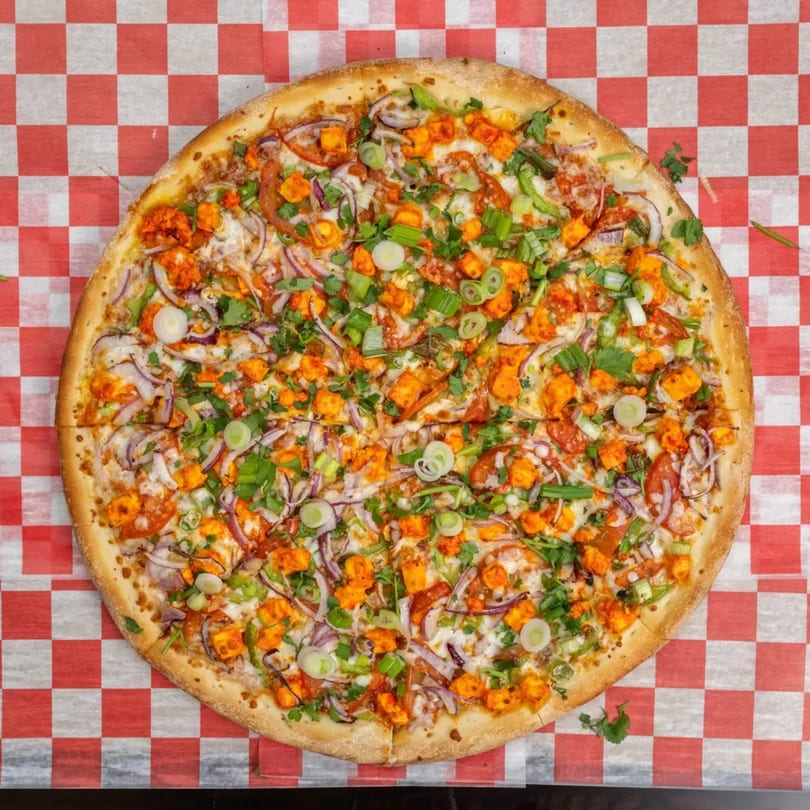 Garlex Pizza & Ribs' chicken tikka pizza, topped with red onions, green onions, and cilantro.