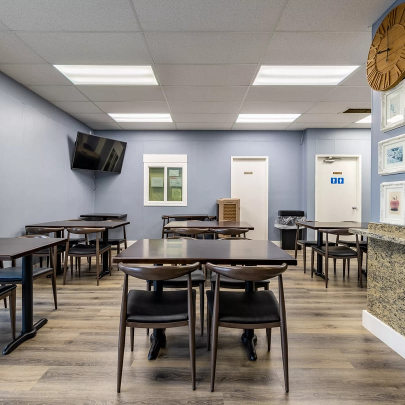 Empty dining room at Garlex Pizza & Ribs with dark tables and chairs, light blue walls, and wood floors.
