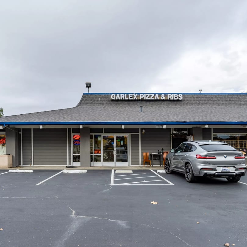 The exterior of Garlex Pizza & Ribs, a gray building with a blue-trimmed roof and a silver car parked outside.