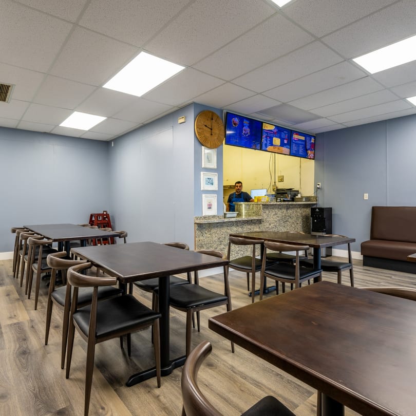 Interior of Garlex Pizza & Ribs, with empty tables, a counter, and a staff member.