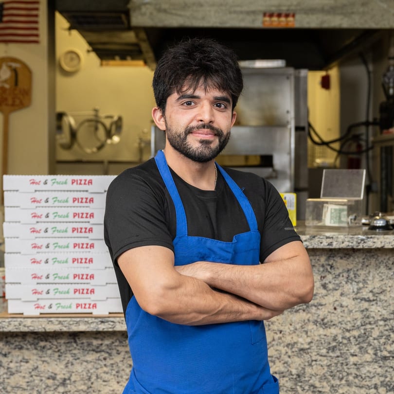Garlex Pizza & Ribs employee in a blue apron standing in front of stacked pizza boxes.