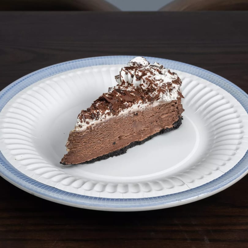 A slice of chocolate pie with whipped cream and chocolate shavings on a white plate.